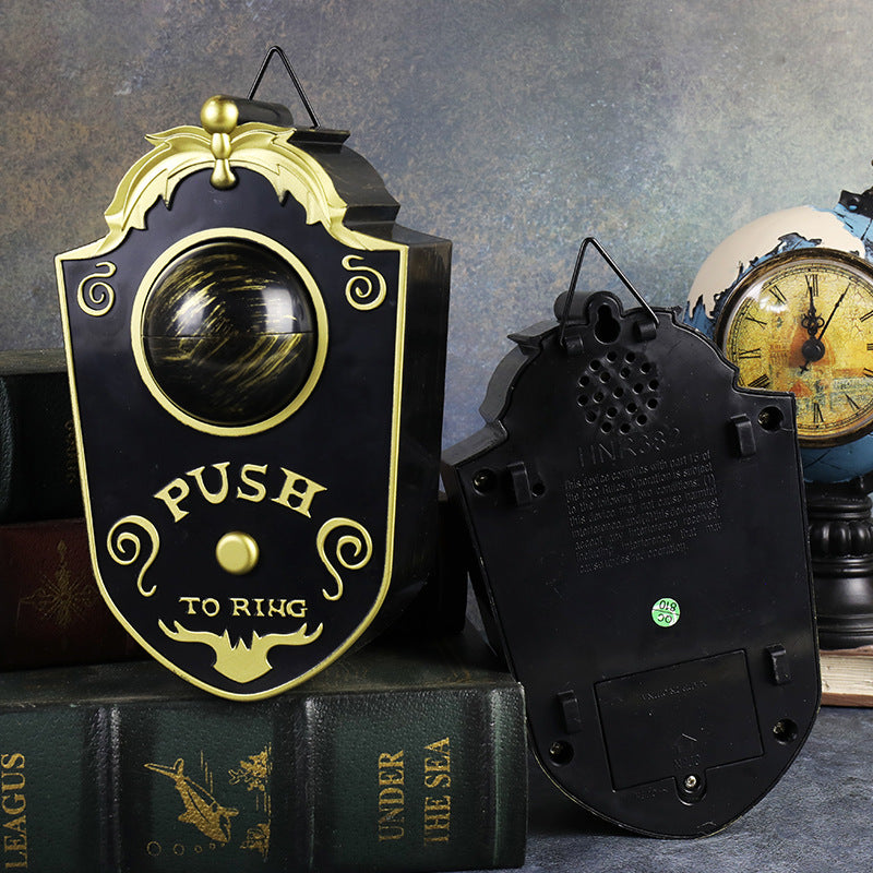 Black Halloween eyeball doorbell prop, front green eye and back showing the wire hook and battery compartment