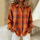 Woman in an orange plaid knit cardigan with red check, shirt collar and white buttons over white trousers
