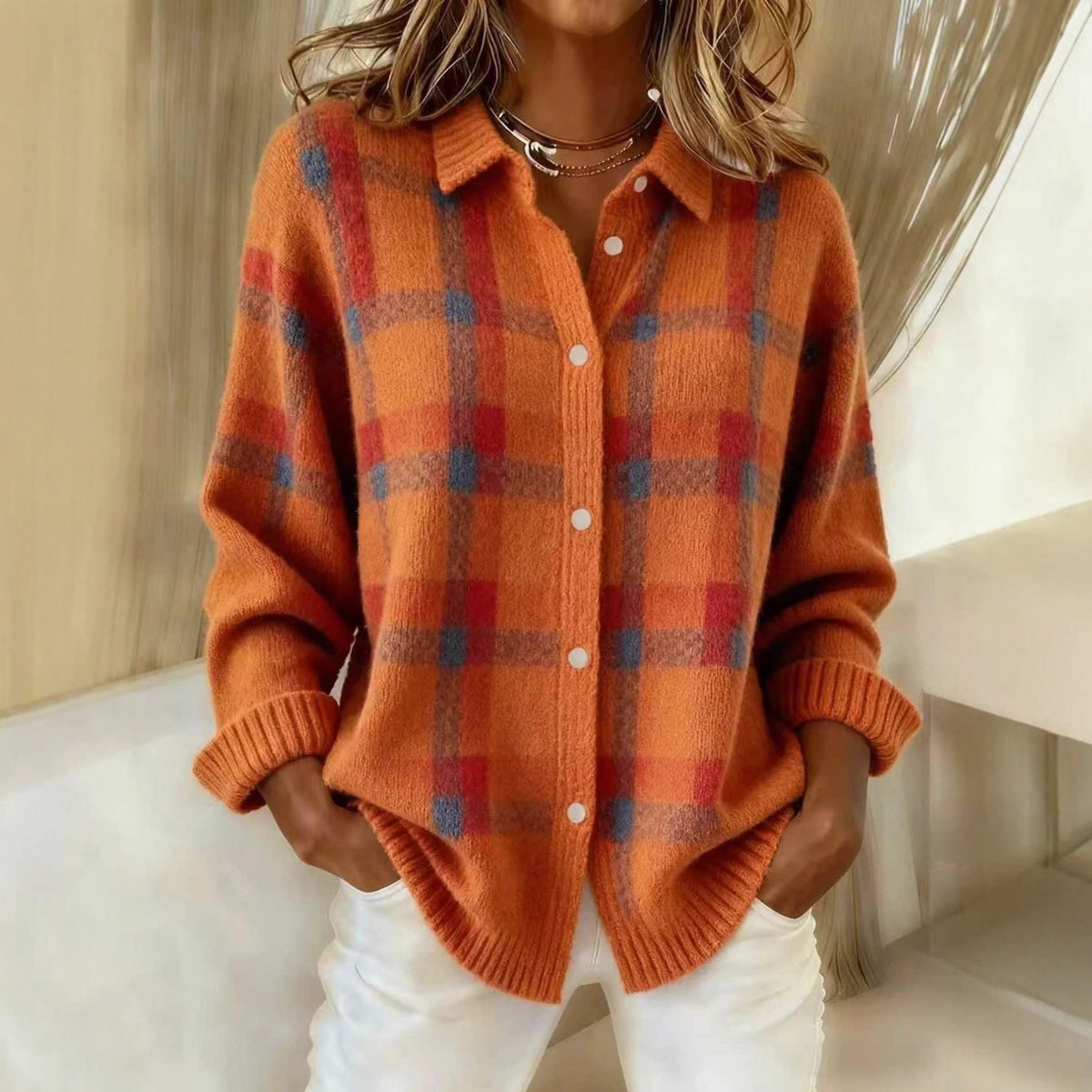 Woman in an orange plaid knit cardigan with red check, shirt collar and white buttons over white trousers