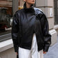 Woman in sunglasses wearing a black moto jacket with an asymmetric front zip and white trousers