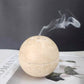 Cream travertine burner sphere with a thin ribbon of incense smoke rising from the drilled crown holes