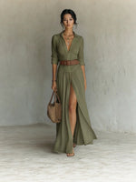 Woman in a dark green long shirt dress with collar, brown belt and a high front slit, full length front view
