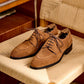 Camel suede derby shoes angled on woven seating, brown laces threaded through four eyelets