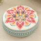 Round cushion with a coral, red and orange lotus print on a cream top and a teal woven border
