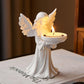 Angel figure holding a lit tea light in its dish on a styled shelf
