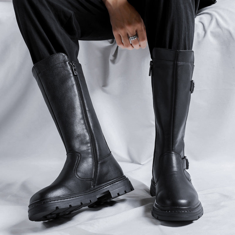 Tall black boots with buckle straps and a side zipper, worn standing, with chunky lugged rubber soles