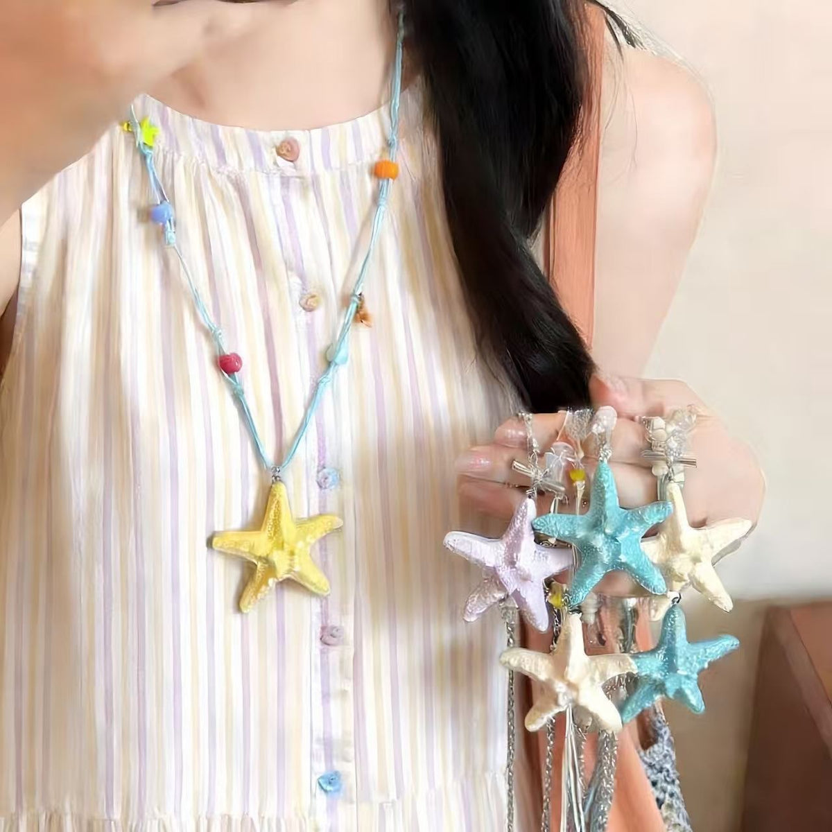 Yellow resin starfish cord necklace worn over a striped dress with a hand holding starfish pendants