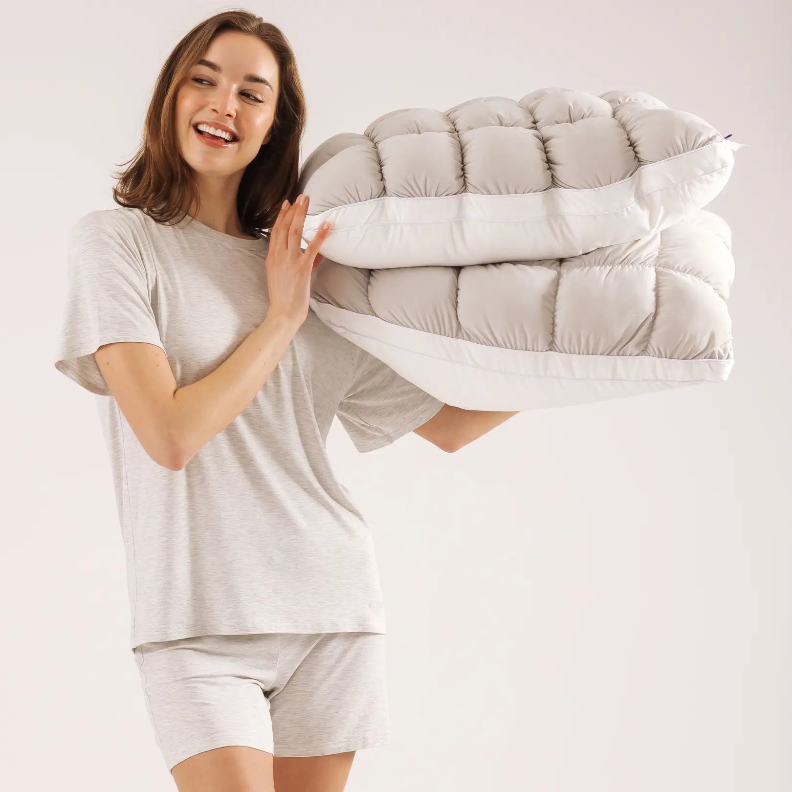 Woman holding two gray puff grid bed pillows against a plain studio backdrop