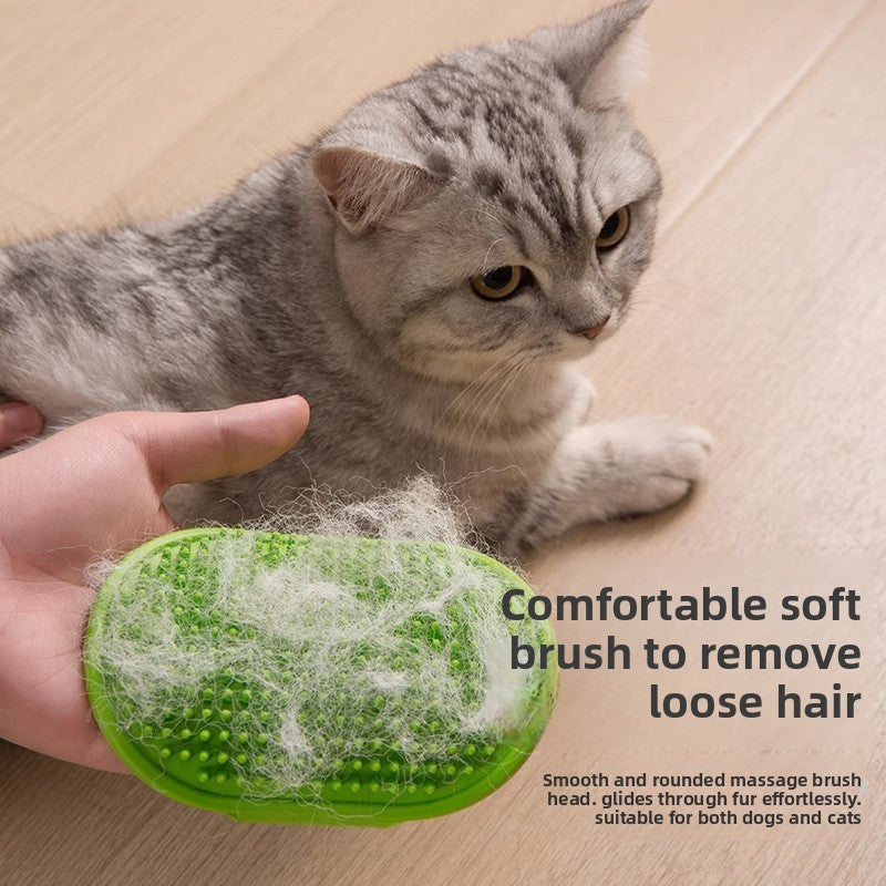 Grey cat beside a hand holding the green groomer brush matted with lifted loose hair pulled from the coat