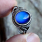 Color changing cabochon ring held up showing blue stone and braided silver frame