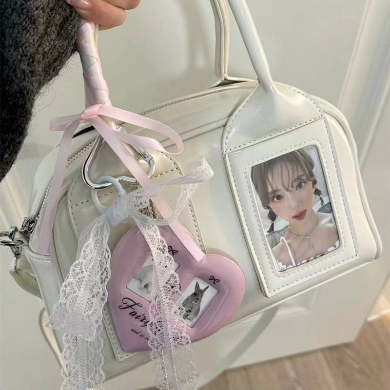 White glossy crossbody bag with two top handles and a photo card in its clear front window