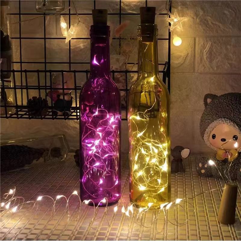 Copper wire LED string lights inside two bottles, pink and warm white glow, on a shelf as decoration