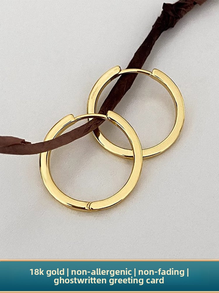 Hand holding one of the gold hoops between two fingers in daylight