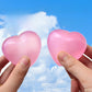 Two frosted pink heart squeeze toys held up against a blue sky, light passing through them