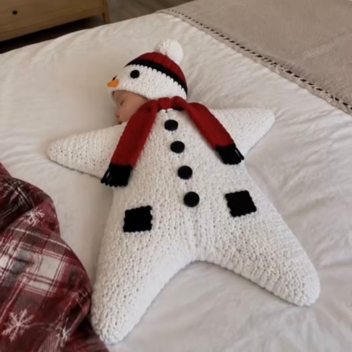 Baby in a white knitted star sleeping bag with a snowman hat, snowman design shown, not one of the four options