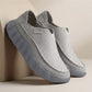 Pair of light gray perforated slip-on loafers with a slate gray scalloped sole leaning on a beige backdrop