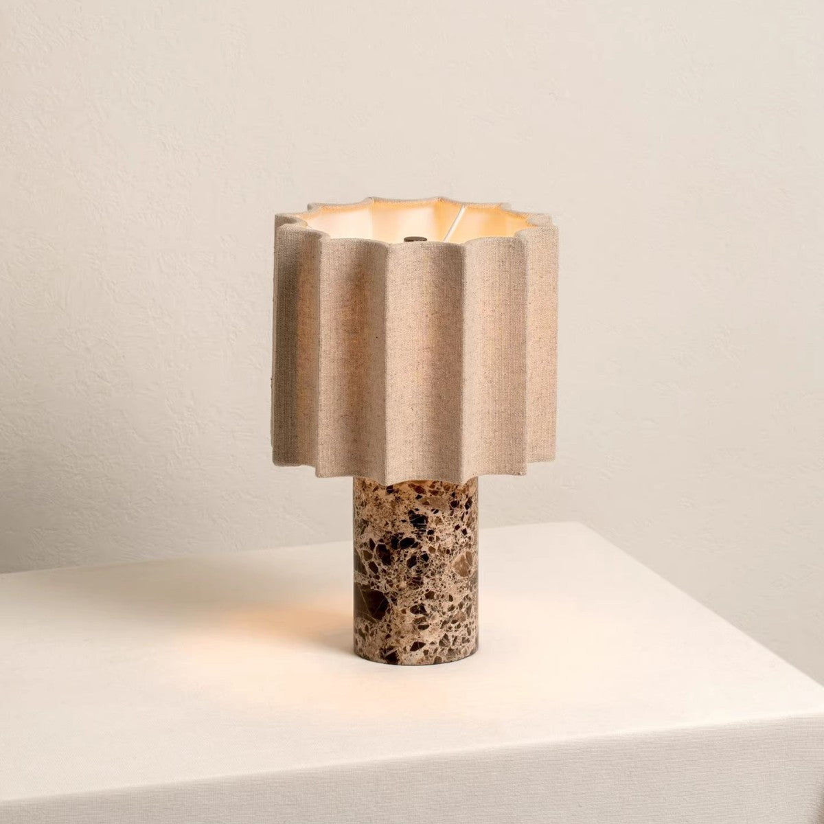 Rechargeable marble table lamp with a brown stone base and fluted linen shade glowing warm