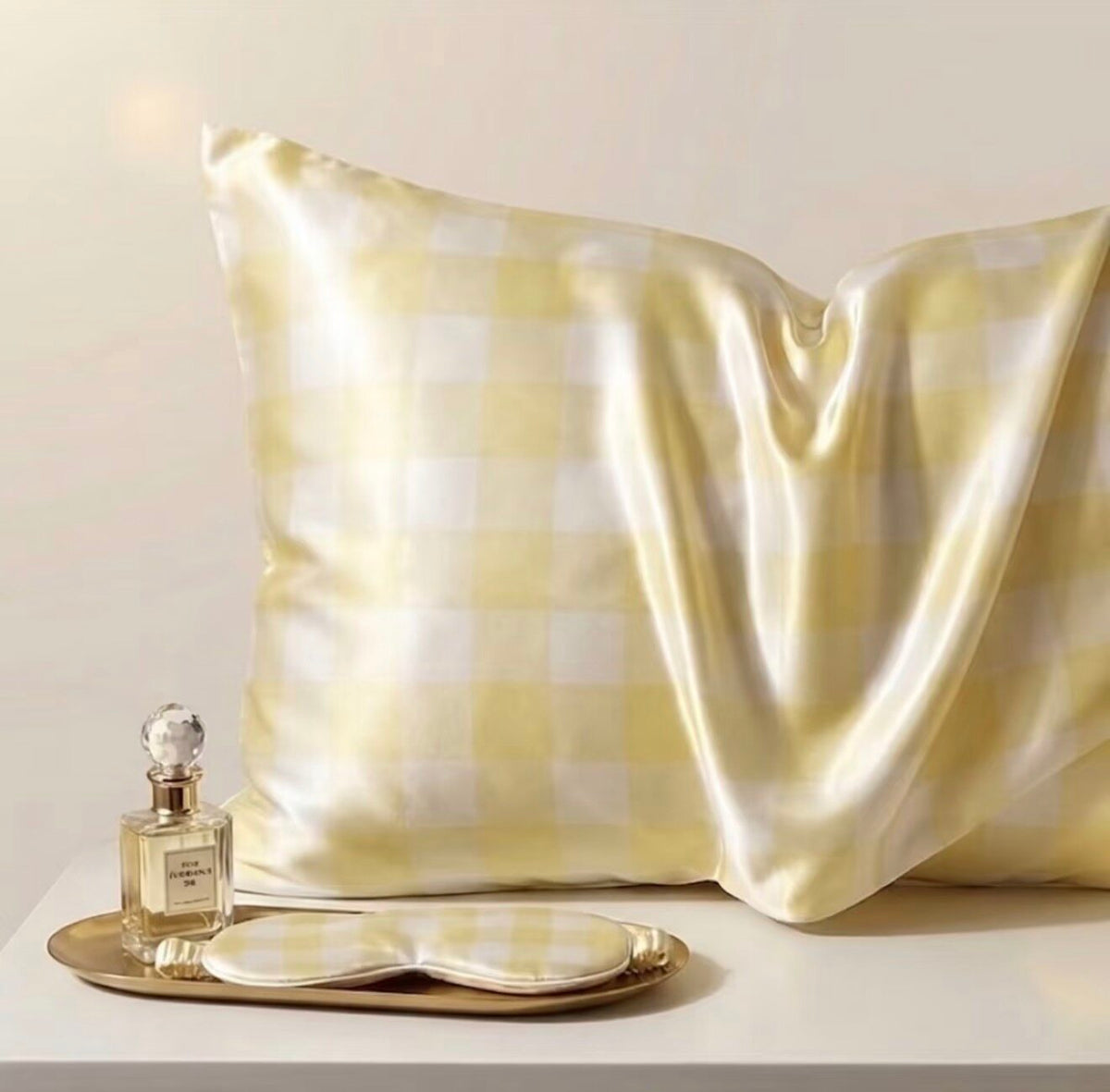 Yellow check silk pillowcase in pale gingham with a perfume bottle and sleep mask