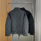 Back view of a washed gray quilted jacket beside a black one on a rack with hem cords hanging down