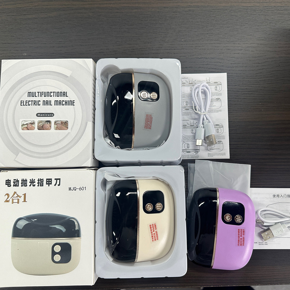 Three electric nail clipper units in gray, beige and purple with boxes, USB cables and printed manuals on a dark table