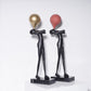Balloon figure sculpture with a gold toned balloon above a matte black body on a veined marble base