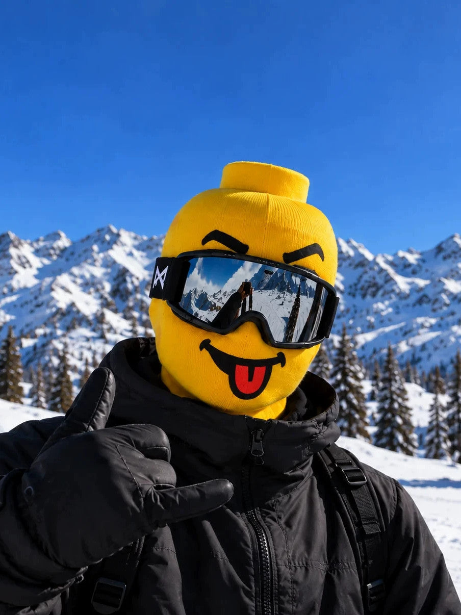 Yellow block head printed face cover with tongue out and ski goggles, thumb up in black ski gloves