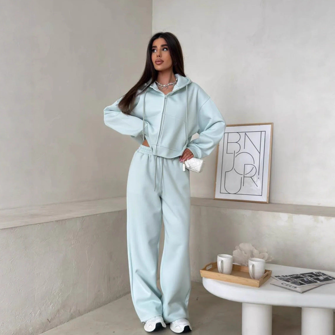 Pale aqua cyan zip front hooded sweatshirt and matching wide leg trousers set, model with a small white bag in hand