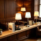 White shade table lamps in gold, silver and black lit along a wood panelled lounge
