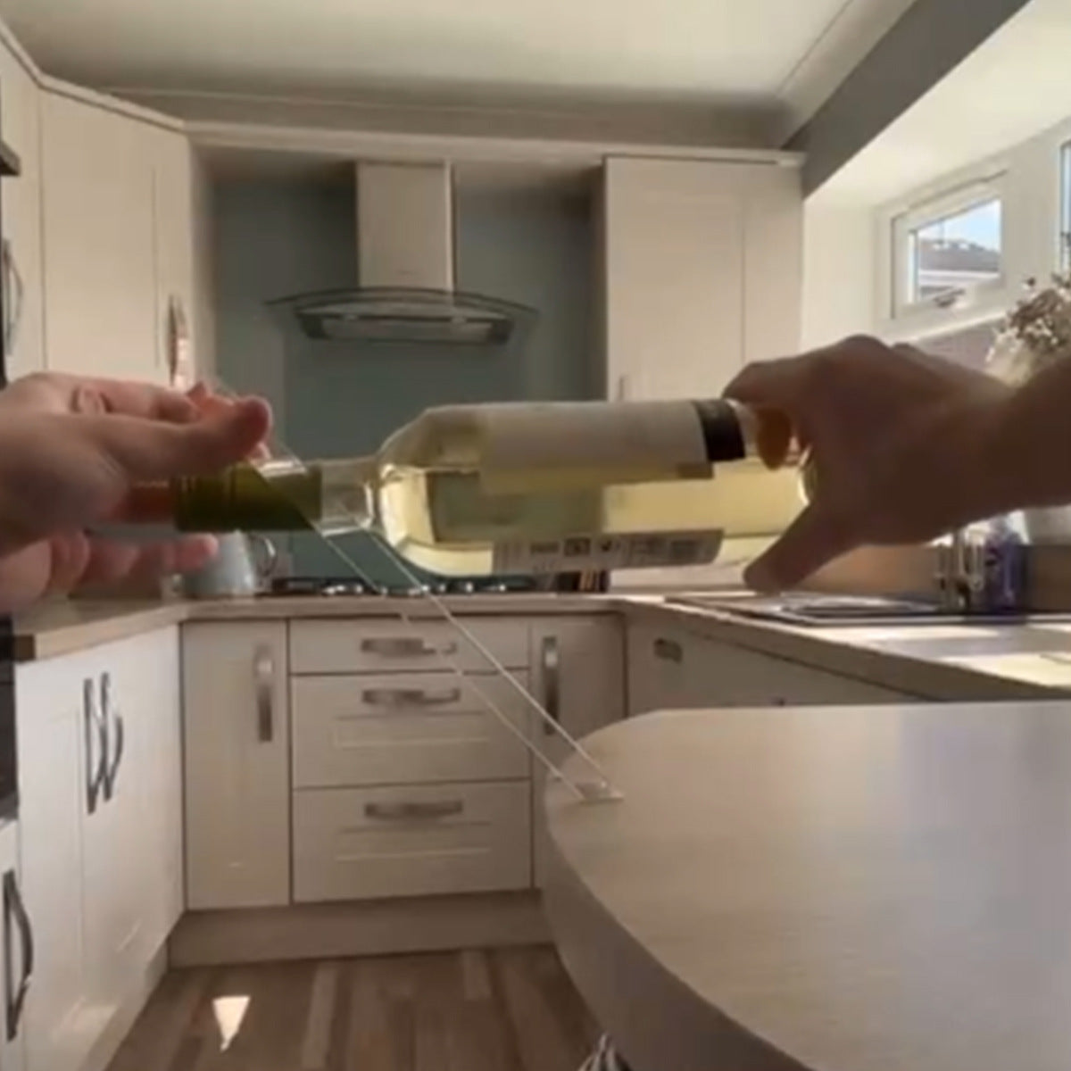 Hand placing a white wine bottle onto a slanted clear acrylic holder on a kitchen counter