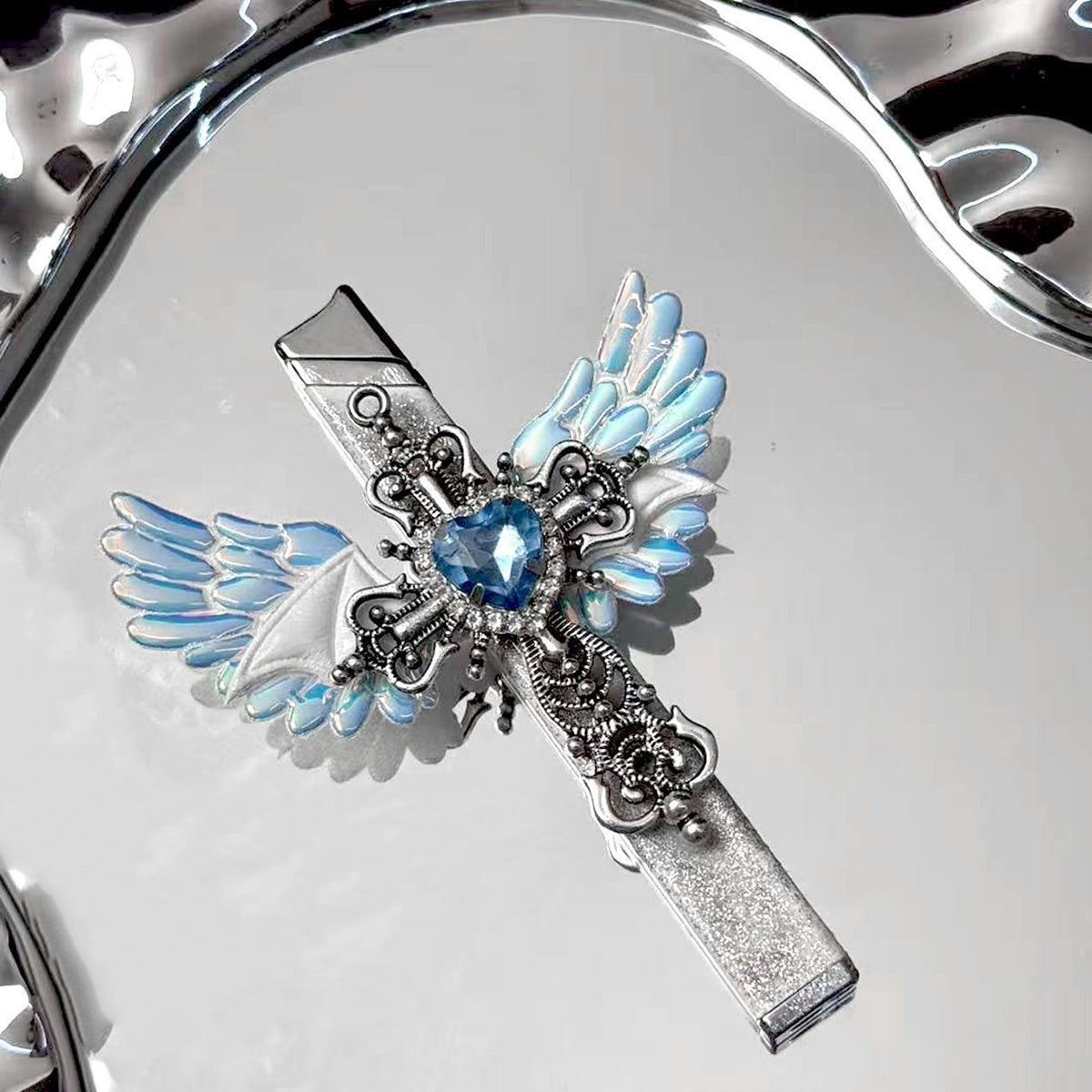 Angel wings cross lighter with iridescent blue wings and a blue heart rhinestone on a silver mirror tray
