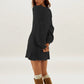 Back view of a woman in a black cable knit sweater dress with long full sleeves and brown boots