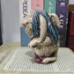 Side profile of resin troll figurine with hand raised in a thoughtful pose