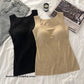 Black and nude seamless square neck tank tops flat lay on white bedding with jeans and a candle