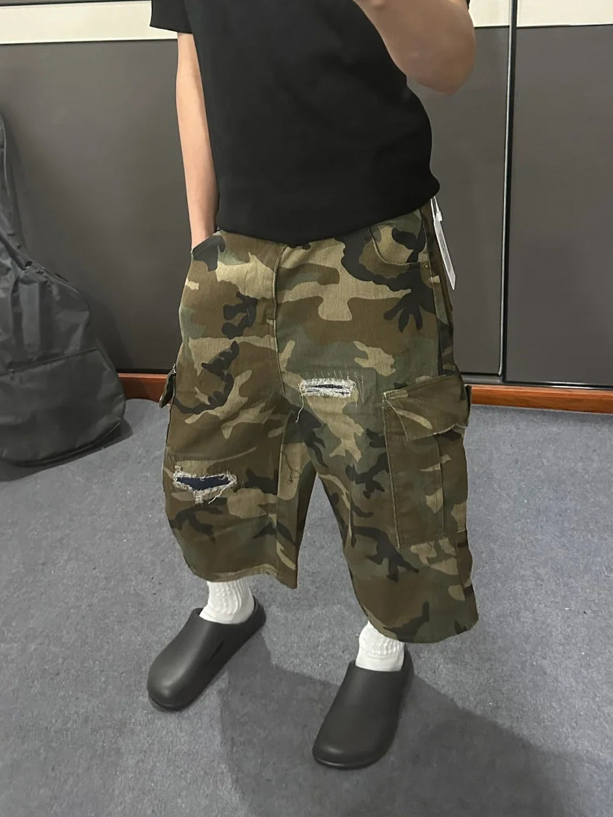 Angled view of the loose camo cargo shorts with a side cargo pocket, a rip and a navy patch on the leg
