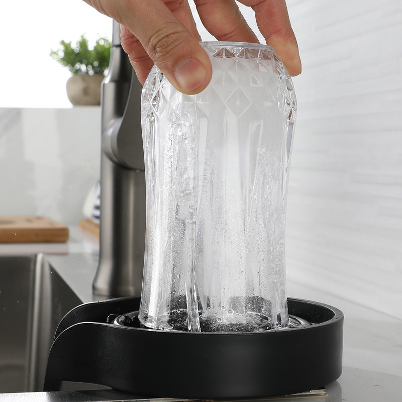 Hand pressing a clear glass onto a black ABS countertop glass rinser as water jets up inside