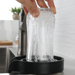 Hand pressing a clear glass onto a black ABS countertop glass rinser as water jets up inside