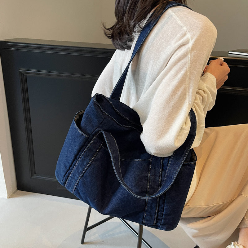 Dark blue denim shoulder tote carried on the shoulder, twin straps and soft slouching washed denim body