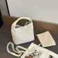 White woven PU bucket bag with the crossbody strap and matching woven zip pouch laid out beside it