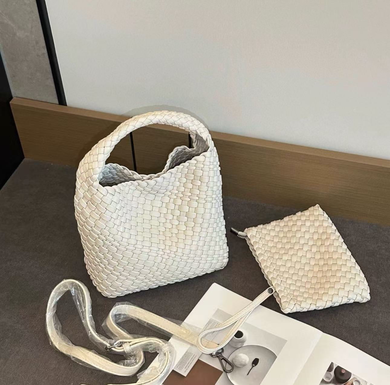 White woven PU bucket bag with the crossbody strap and matching woven zip pouch laid out beside it