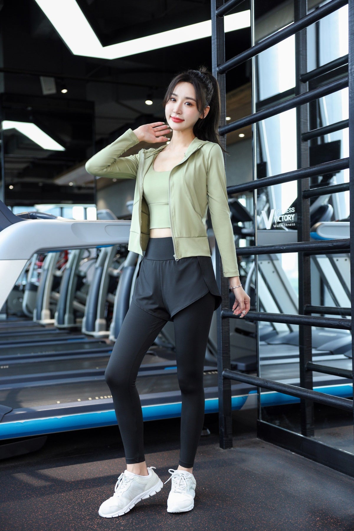 Model wearing the green hooded jacket, cropped bra and grey overlay leggings at the gym