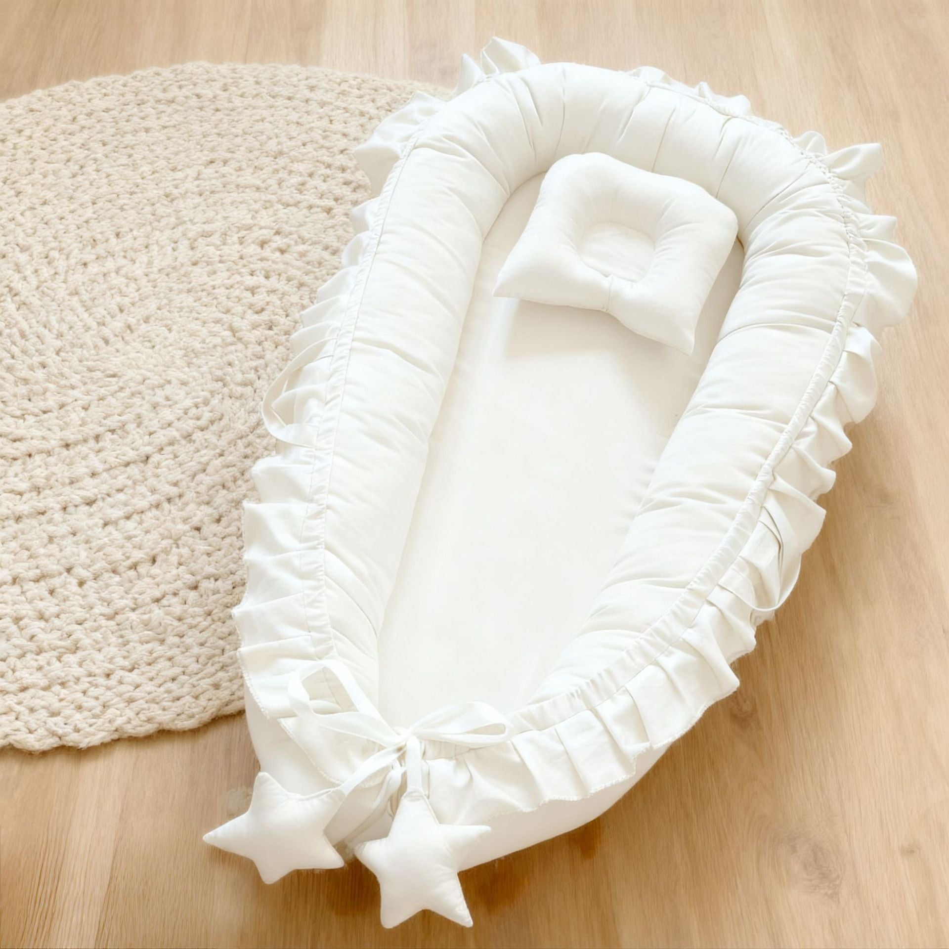 Cotton baby nest shown in white with a ruffle trim and adjustable foot cord