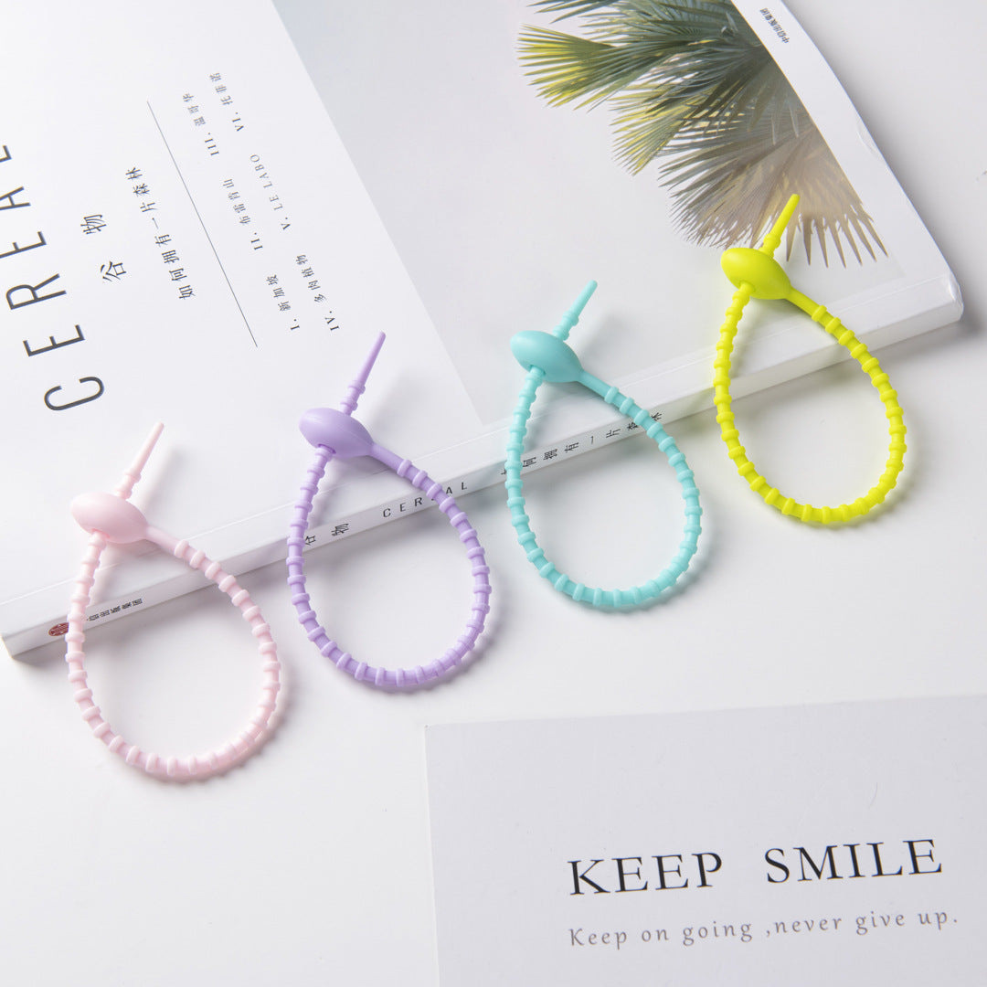 A few pastel silicone tadpole cable ties resting on open books in soft daylight