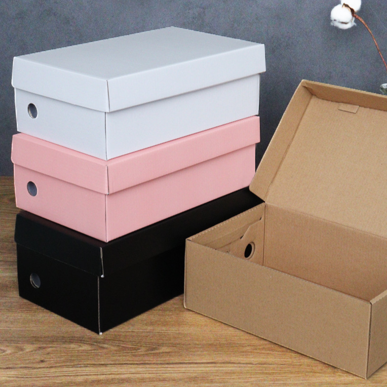 Stack of white, pink and black cardboard shoe boxes with lids beside an open kraft box on a wooden floor