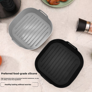 Gray and black silicone air fryer liner trays with ridged bases beside a plate of cooked bacon