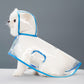 Small white dog seated in a clear EVA hooded rain poncho with sky blue trim, studio three quarter view