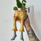 Resin lower body planter with dangling legs holding a small plant, painted style