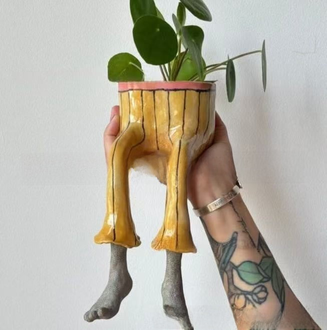 Resin lower body planter with dangling legs holding a small plant, painted style