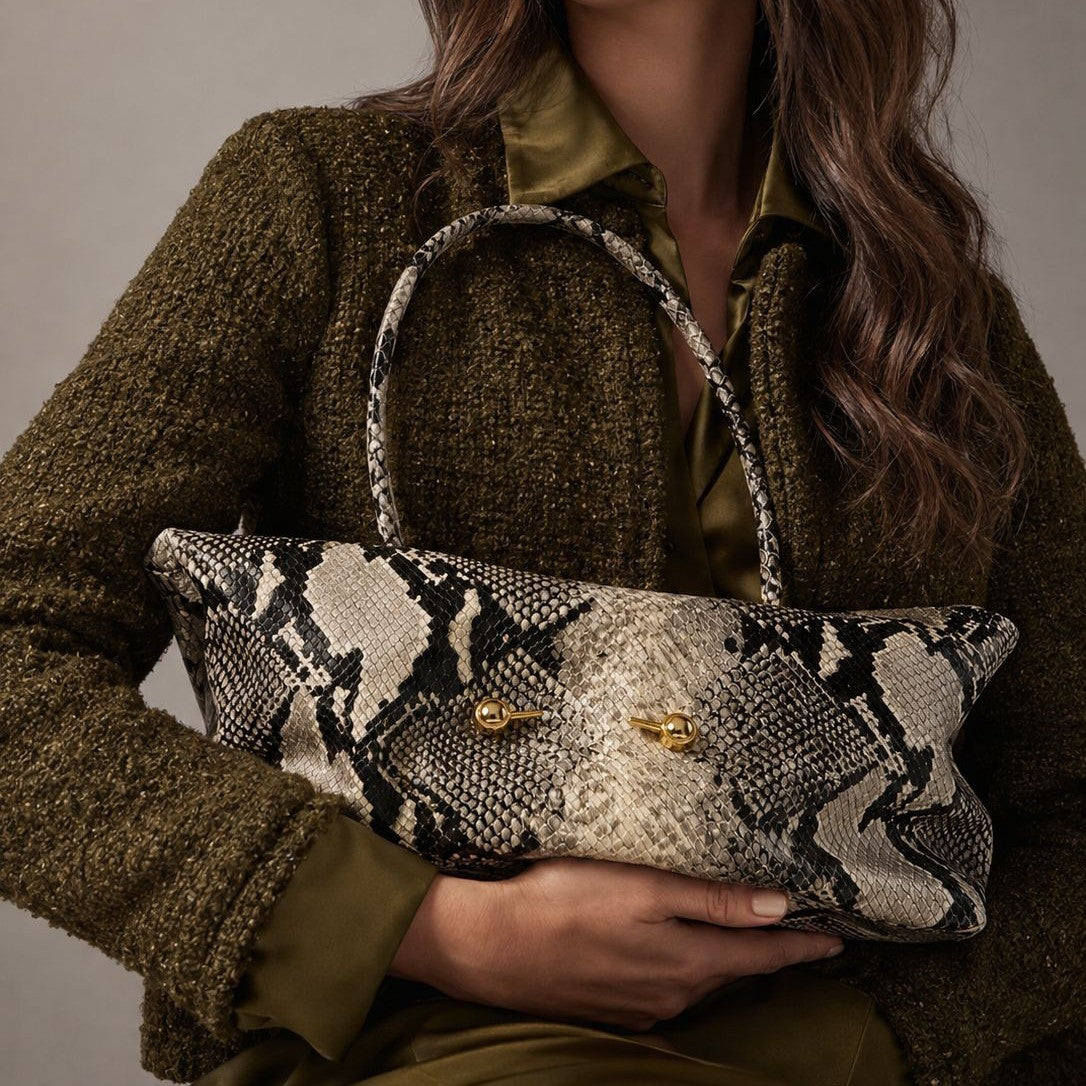 Woman in an olive tweed jacket holding a snake print shoulder bag by the round handle