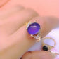 Close-up of a gold-tone ring with a deep purple oval mood stone and clear accent stones on the shoulders