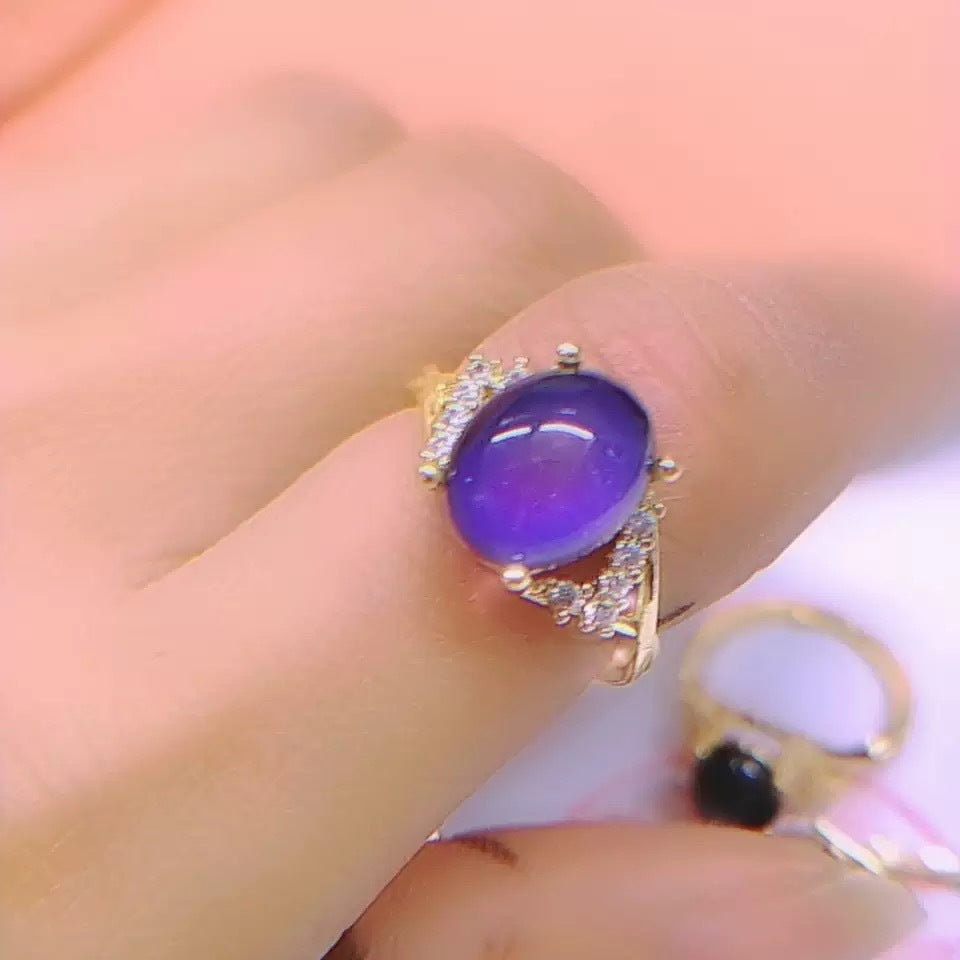 Close-up of a gold-tone ring with a deep purple oval mood stone and clear accent stones on the shoulders
